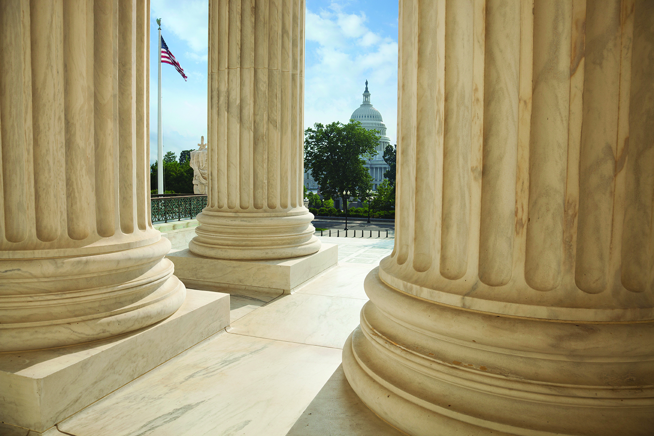 Close up of the columns  of the Supreme Court building with an American flag and the US Capitol in the background